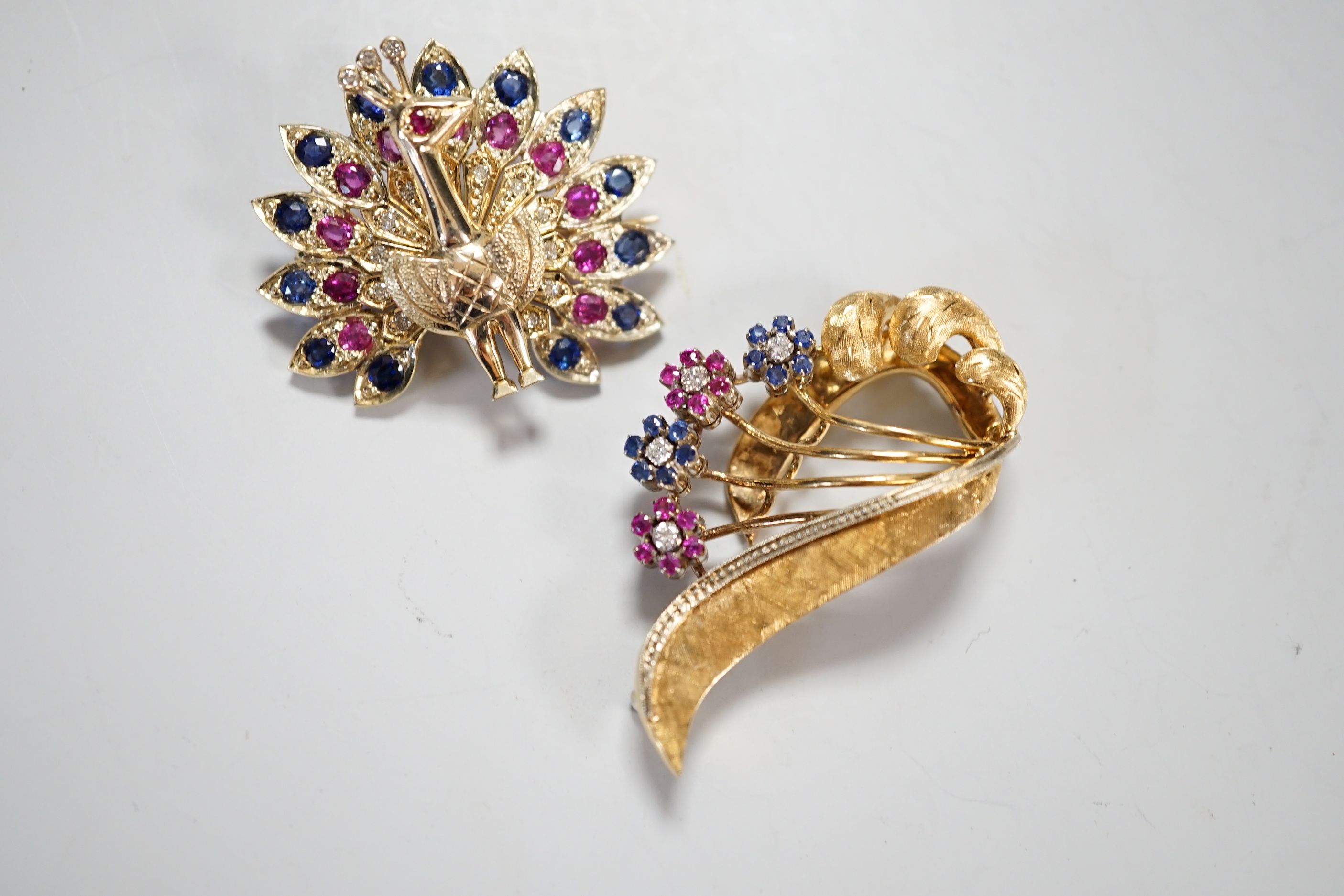 A modern Italian 18k, ruby, sapphire and diamond set floral spray brooch, 42mm and a yellow metal and gem set peacock brooch, gross weight 25.6 grams.